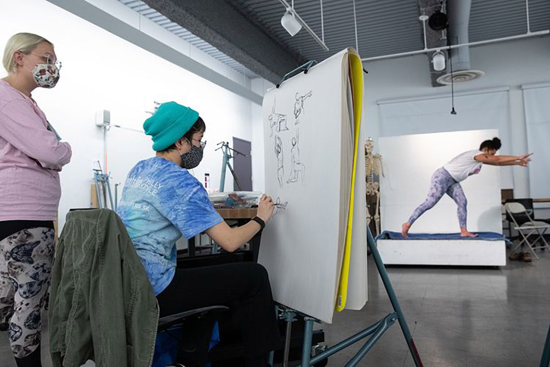 Student drawing posing model