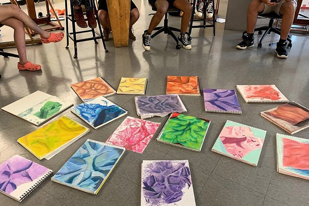 Students sitting around drawings laying on floor
