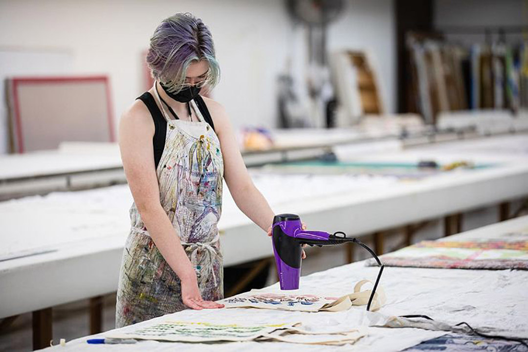 Student drying artwork with blow dryer