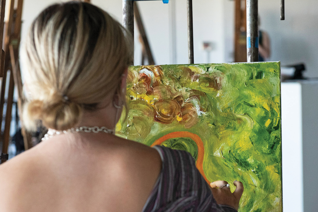 Over the shoulder photo of a student working on a green abstract painting